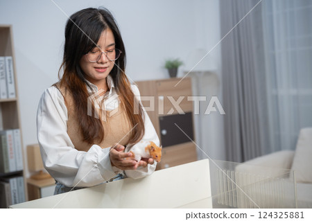 Young woman holding a small hamster in a cozy modern room with bright natural light and soft furnishings for a warm atmosphere and joyful pet relationship Young woman holding a small hamster in a cozy modern room with bright natural light and soft furnishings for a warm atmosphere and joyful pet relationship 124325881