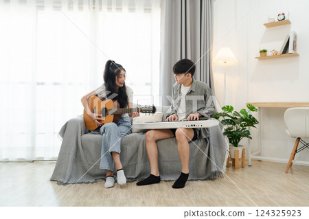 Asian Young couple enjoying musical moments at home, playing guitar and keyboard together in cozy living space with natural light streaming through windows Asian Young couple enjoying musical moments at home, playing guitar and keyboard together in cozy living space with natural light streaming through windows 124325923