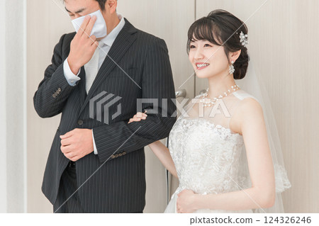 A bride walking down the aisle to the chapel where the groom is waiting at the wedding venue; the bride's father wiping away her tears A bride walking down the aisle to the chapel where the groom is waiting at the wedding venue; the bride's father wiping away her tears 124326246