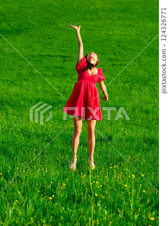Woman in an elegant pink dress jumping on the green grass at sunset 124326771