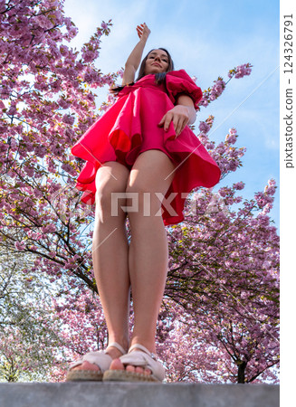 Young woman with arms raised enjoying nature in a cherry tree orchard under the blue sky 124326791