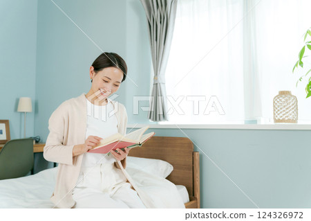 Woman sitting by the bed and reading a book 124326972