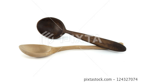 Two wooden spoons, one light and one dark, are artfully arranged on a white surface. 124327074
