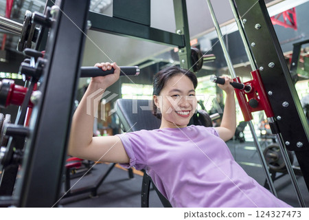 Chinese east asian woman training on chest press machine at the gym. Fitness exercise and healthy lifestyle concept Chinese east asian woman training on chest press machine at the gym. Fitness exercise and healthy lifestyle concept 124327473