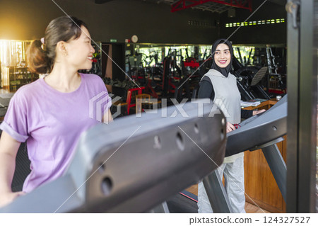 Chinese east asian and arab middle eastern muslim women training on treadmill machines at the gym. Fitness exercise and healthy lifestyle concept 124327527