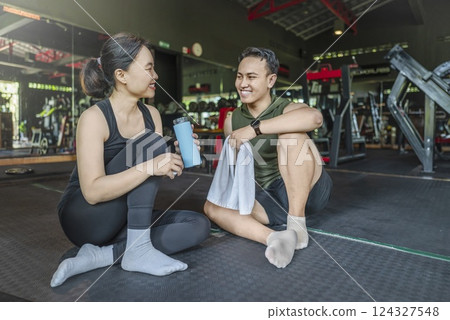 Chinese east asian woman taking a break after exercising with Indonesian southeast asian personal trainer man at the gym. Fitness exercise and healthy lifestyle concept Chinese east asian woman taking a break after exercising with Indonesian southeast asian personal trainer man at the gym. Fitness exercise and healthy lifestyle concept 124327548
