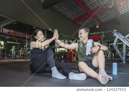 Chinese east asian woman taking a break after exercising with Indonesian southeast asian personal trainer man at the gym. Fitness exercise and healthy lifestyle concept 124327553