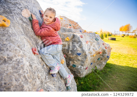 Little girl climbing an artificial climbing wall in a playground, developing strength and coordination Little girl climbing an artificial climbing wall in a playground, developing strength and coordination 124329972