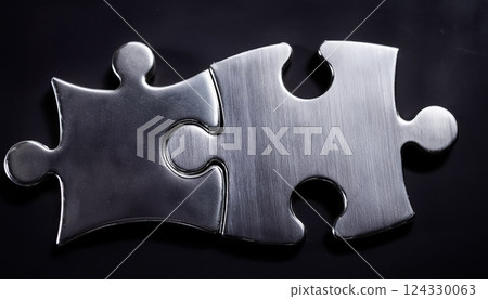 Two interlocking metal puzzle pieces on a black background 124330063