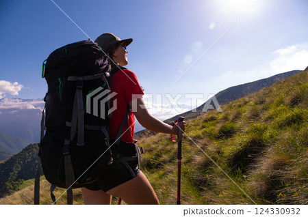 Young beautiful tourist in a cap climbs to the top of the mountain. Active woman enjoys the beautiful landscape of majestic mountains. Travel, adventure. Active lifestyle concept Young beautiful tourist in a cap climbs to the top of the mountain. Active woman enjoys the beautiful landscape of majestic mountains. Travel, adventure. Active lifestyle concept 124330932