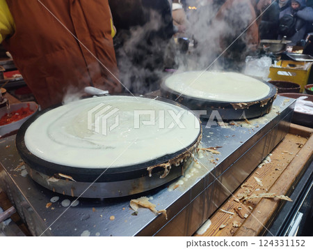 Frying pancake. Making pancakes with lot of steam outdoors. Persona preparing large round pancake on frying pan close-up. Cooking food on street. Cooking street food fried dough. Festivities. 124331152