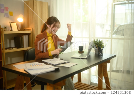 Excited young businesswoman celebrating a positive result while looking at digital tablet Excited young businesswoman celebrating a positive result while looking at digital tablet 124331308