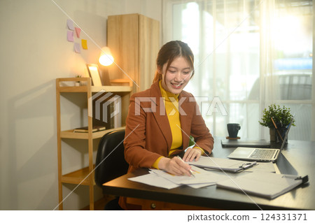 Smiling businesswoman sitting at desk with laptop, reviewing graphs and statistics Smiling businesswoman sitting at desk with laptop, reviewing graphs and statistics 124331371