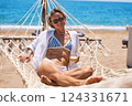 Enjoying summer vacation. Young happy woman relaxing while lying in the hammock on the sandy beach 124331671