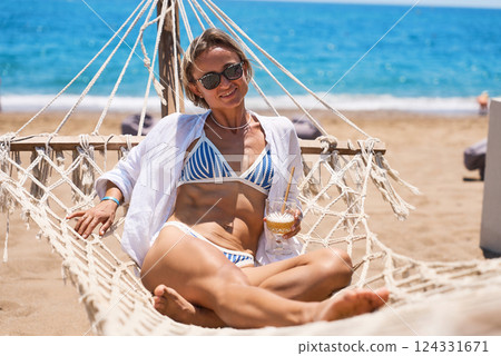 Enjoying summer vacation. Young happy woman relaxing while lying in the hammock on the sandy beach 124331671