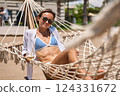 Enjoying summer vacation. Young happy woman relaxing while lying in the hammock on the sandy beach 124331672