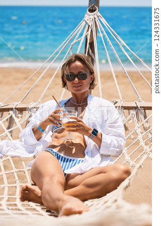 Enjoying summer vacation. Young happy woman relaxing while lying in the hammock on the sandy beach 124331675