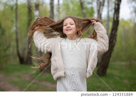 A beautiful girl with long hair in a fur coat poses against the background of a birch grove. 124331884