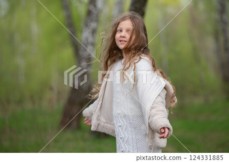 A beautiful girl with long hair in a fur coat poses against the background of a birch grove. 124331885