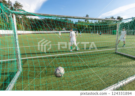 Football pitch with green net and football in goal. Man in white t-shirt standing in front of net Football pitch with green net and football in goal. Man in white t-shirt standing in front of net 124331894
