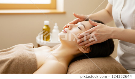 Image of a young Japanese woman comfortably receiving a facial massage at a salon 124332644