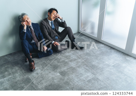 A pair of middle-aged male business people sitting on the floor in an office 124333744