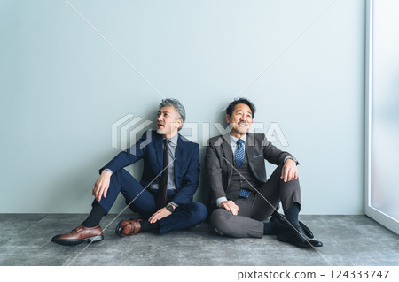 A pair of middle-aged male business people sitting on the floor in an office 124333747