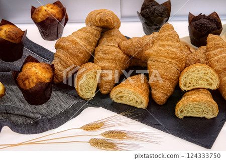 Fresh crispy croissants and muffins on table in cafe, top view. Fresh various pastries in bakery showcase. 124333750