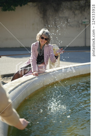 Woman Splashes Water Playfully at Fountain 124333918
