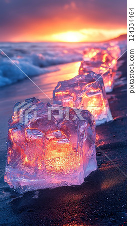 Chunks of ice gleam on Iceland's black sand beach as the sun sets, creating a magical display of light. 124334464