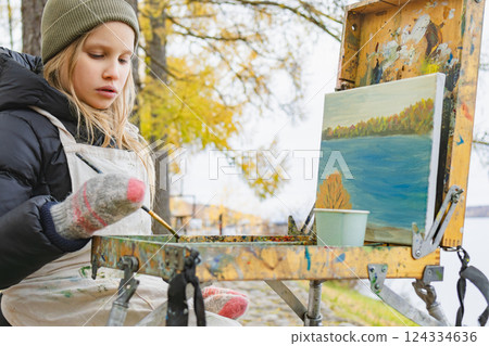 Girl wearing warm clothing painting autumn landscape outdoors 124334636