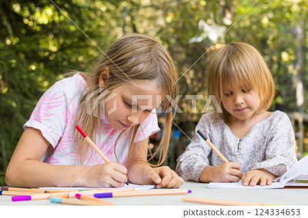 Sisters engaged in creative drawing with fineliners in a summer garden 124334653