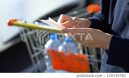 Customer hold receipt bill. Buyer checks. Shopping cart on background. Paper receipt on shopping supermarket. Expensive total. Cash register. Money spending on Hypermarket. Family budget. Check bill. Customer hold receipt bill. Buyer checks. Shopping cart on background. Paper receipt on shopping supermarket. Expensive total. Cash register. Money spending on Hypermarket. Family budget. Check bill. 124334762