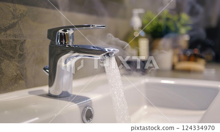 a modern bathroom sink with a chrome faucet from which water and steam come out 124334970