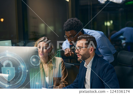 Team Collaborating on Cybersecurity Solutions at Night with Digital Interfaces and Lock Symbol Team Collaborating on Cybersecurity Solutions at Night with Digital Interfaces and Lock Symbol 124336174