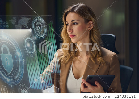 Professional Woman Analyzing Cybersecurity Data on Futuristic Digital Interface in Office 124336181