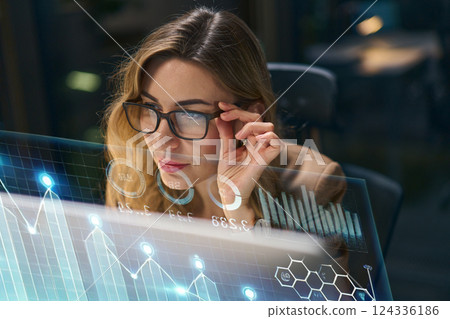 Focused Businesswoman Analyzing Digital Data on a Transparent Interactive Screen at Night 124336186