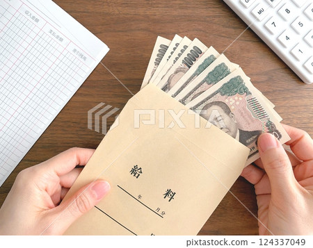 A woman's hand taking out bills from a pay envelope on a desk 124337049