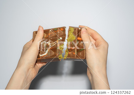 Famous Dubai chocolate with pistachio, tahini and kadaif broken in woman's hands. Confectionery handmade sweets, chocolatier 124337262