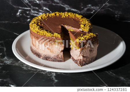 Sliced chocolate Dubai cheesecake with pistachio paste and kataifi dough filling covered in chocolate ganache on white plate. Black background. Indulgence, gourmet desserts, art of culinary 124337281
