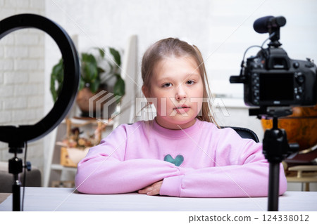 A beautiful blonde teenager is broadcasting live. The video blogger has a live broadcast. An annular lamp and a camera during a live broadcast of a video blogger 124338012