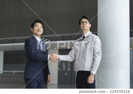 A businessman in a suit and a man in work clothes shaking hands A businessman in a suit and a man in work clothes shaking hands 124338316