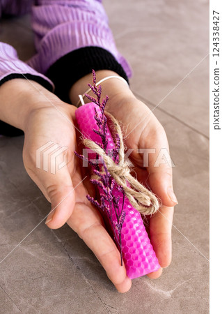 Caucasian female hands holding pink beeswax candle with dried flowers and twine 124338427