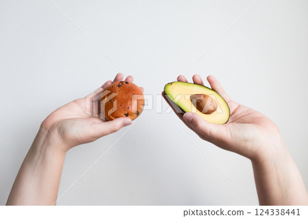 Hands holding avocado halves and chocolate chip cookie against white background Hands holding avocado halves and chocolate chip cookie against white background 124338441