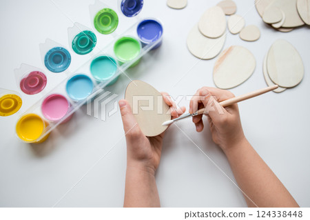 Child painting wooden Easter egg shapes with colorful paint set for crafts 124338448