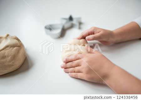 Child shaping dough with cookie cutter on white surface Child shaping dough with cookie cutter on white surface 124338456