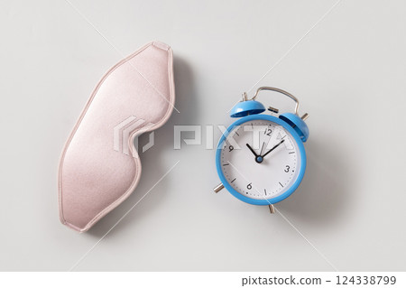 Pink sleeping mask and blue watch, alarm on gray background. Concept of sleep, health care, daily routine and circadian rhythms. View from above. 124338799
