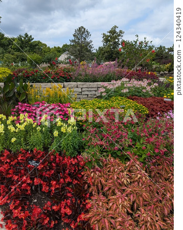 Colorful Flower Garden with Stone Wall and Lush Greenery Under a Cloudy Sky 124340419