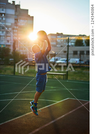 Boy in a blue tracksuit playing basketball Boy in a blue tracksuit playing basketball 124340864