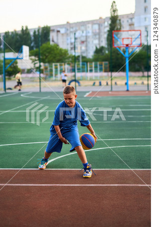 Boy in a blue tracksuit playing basketball 124340879